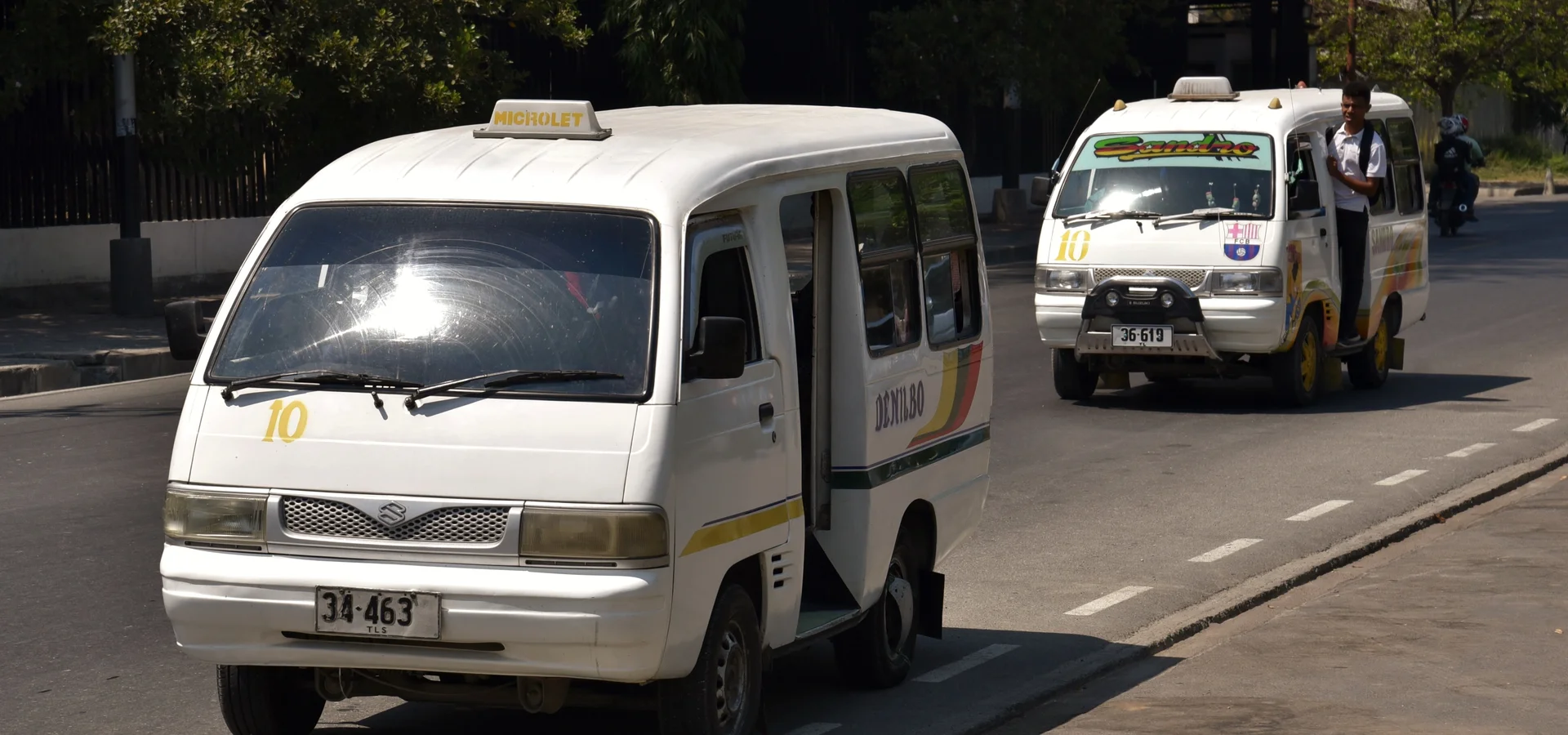 A microlet pulling away from a shaded Dili street stop